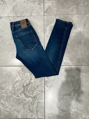 Replay Anbass jeans - Replay jeans, modell Anbass. Jeansen har en cool tvättad look och detaljerade sömmar på bakfickorna. Perfekt för dig som gillar stilrena och moderna jeans. Storleken är i W28.