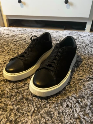 Svarta sneakers från Legend - Säljer ett par svarta sneakers från Legend med snygg platt vit sula och rund tå. Ovandelen är i mocka och tåpartiet i skinn, vilket ger en schysst kontrast. Skorna har snörning och en stilren look som passar till många outfits.
