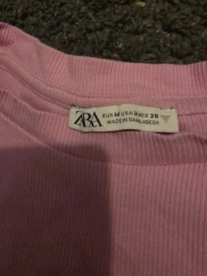 Rosa ribbad topp med volangärm från Zara - Supersöt rosa topp från Zara i ribbad bomull med volangdetaljer på ärmarna. Perfekt för dig som vill ha en feminin och trendig look. Rund halsringning och korta ärmar med extra volym gör den unik och lätt att styla.