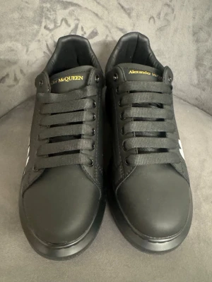 Alexander McQueen Black - Säljer ett par svarta Alexander McQueen sneakers i skinn med bred plattformssula. Skorna har snörning och coolt vitt McQueen-tryck på sidan samt guldfärgad logga på plösen och hälen. Perfekta för dig som vill sticka ut med stilrena men ändå edgy skor.