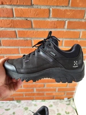 Svarta Haglöfs sneakers med grov sula 36 2/3 - Säljer ett par svarta Haglöfs sneakers med robust och grov sula, perfekt för dig som gillar outdoor och äventyr. Skorna har snörning, rund tå och är tillverkade i slitstarkt skinn och syntetmaterial. Diskret Haglöfs-logga på sidan och meshfoder för extra komfort.