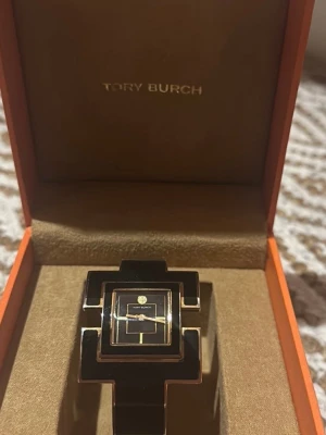 Damklocka - Elegant Tory Burch damklocka med svart och guldfärgad design. Klockan har en stilren urtavla och ett unikt armband.