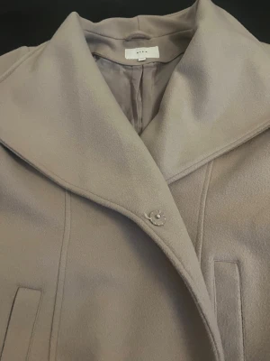 Beige kappa från VILA, strl 44 - Snygg beige kappa från VILA i storlek 44. Jackan har bred krage, diskreta fickor och stängs med knapp framtill. Materialet är mjukt och känns lyxigt, perfekt för kyliga dagar. Fodret är ljust och har små prickar för extra detalj. Bättre bilder kan skickas ifall efterfrågat!