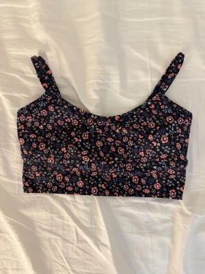 Blommig träningstopp från Aim'n - Supersöt träningstopp från Aim'n med blommigt mönster i rosa, lila och vitt på mörkblå botten. Toppen har smala axelband och är croppad i modellen.