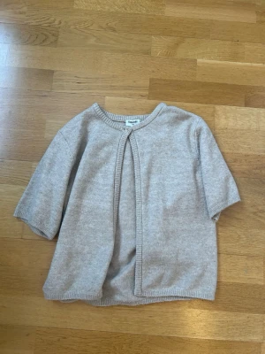 Beige kortärmad kofta från Kappahl - Supermjuk och stilren beige kofta från Kappahl med korta ärmar och rund hals. Koftan är stickad i ett tunt material och har en enkel knapp framtill. Perfekt att slänga över ett linne eller t-shirt för en chill look. Nypris typ 250 