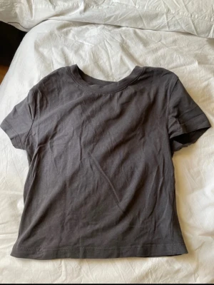 Mörkgrå t-shirt från Divided - Säljer en enkel och stilren mörkgrå t-shirt från Divided i storlek M. T-shirten har rund hals och korta ärmar, perfekt för en chill och avslappnad look. Materialet är mjuk bomull som känns skönt mot huden.