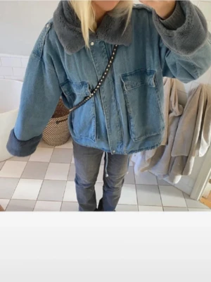 Oversized jeansjacka med teddykrage  - Säljer en oversized jeansjacka i blått med mjuk grå teddykrage och muddar. Jackan har stora fickor framtill och stängs med knappar. Perfekt för dig som gillar chill och streetstyle. Passar dig som vill ha en unik och cozy look. Pris kan diskuteras men köp för 1200 