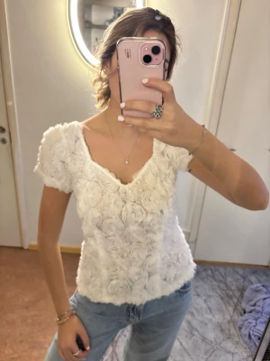 Vit blommig topp från Ida Sjöstedt - Superfin vit topp från Ida Sjöstedt med 3D-blommor över hela tyget. Toppen har v-ringning, korta puffärmar och är gjord i ett tunt, spetsliknande material. Använd två gånger totalt💓💓nypris: 2500kr