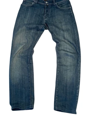 Blå jeans från Corneliani ID - Snygga blå jeans från Corneliani ID med klassisk femficksdesign och broderad C-logga på bakfickan. Jeansen har raka ben och normal passform, tillverkade i mjukt denim med subtila slitningar. Italiensk kvalitet och stilren look. Storlek W31 L32.