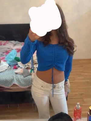 Blå croppad topp med snörning - Köptes för 400kr säljs för 120kr. Säljer en blå croppad topp med långa ärmar och snygg snörning framtill. Toppen är ribbad och har en tight passform som framhäver midjan. Perfekt att styla med höga jeans eller kjol för en trendig look.