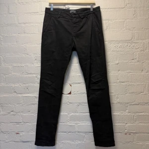 Dondup Gaubert Chinos - Svarta chinos från Dondup, tillverkade i Italien. Byxorna har en slim fit passform med sidfickor fram och knäppning bak. Diskret D-logga vid bakfickan ger en snygg detalj. Mycket fint skick.