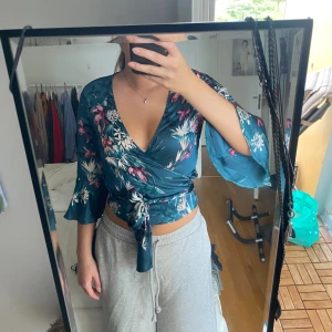 Blommig omlottopp från Gina Tricot - Supersnygg blommig omlottopp från Gina Tricot i blått med vita och rosa blommor. Croppad modell med knyt i midjan och vida trekvartsärmar. Perfekt för dig som vill ha en trendig och färgglad look!