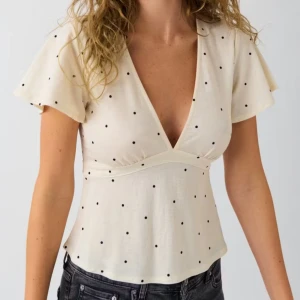 Prickig omlottopp med knyt i midjan - Supersöt ljus topp med svarta prickar, v-ringning och korta ärmar. Använt ca 2 gånger och får ingen användning🥰