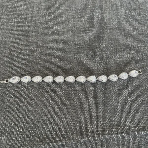 Glittrigt armband med droppformade stenar - Säljer ett riktigt snyggt armband med stora, droppformade glittriga stenar i silverfärgad infattning. Perfekt statement piece om du vill sticka ut och få extra bling på handleden. Låset är diskret och armbandet känns lyxigt och trendigt.