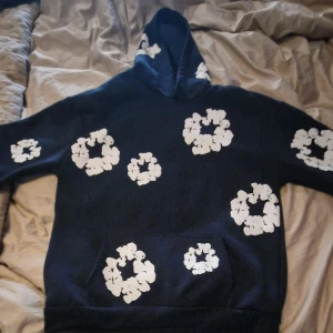 Mörkblå denim tears hoodie - Säljer en mörkblå hoodie med stora vita blommönster över hela tröjan, även på huvan. Tröjan har klassisk känguruficka framtill och är långärmad. Perfekt för dig som vill sticka ut med en cool och unik stil.
