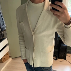 Stickad kavaj john Henric  - Snygg beige stickad kavaj från John Henric med klassisk kavajkrage och tre utanpåfickor. Oerhört snygg beige/krämvit stickad kavaj från John Henric, väldigt bra skick 