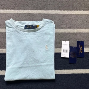 Ljusblå t-shirt från Polo Ralph Lauren - Snygg ljusblå t-shirt från Polo Ralph Lauren med klassisk broderad logga på bröstet. T-shirten är i mjuk bomull och har en normal passform med korta ärmar och rund hals. Perfekt basic-plagg med stilren look.