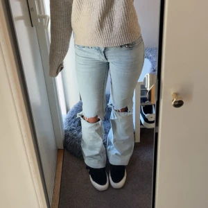 Ljusblå jeans med hål vid knäna - Säljer ett par ljusblå jeans med raka ben och snygga slitningar vid båda knäna. Jeansen är i ett mjukt denimtyg. Perfekta för en trendig look. Dom är även upp sydda så dom passar perfekt för dom som är runt 160 cm långa.