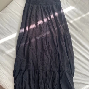 Svart långkjol med resårmidja - Svart långkjol med skön resår i midjan och flera volanger som ger ett avslappnat och flowigt intryck. 