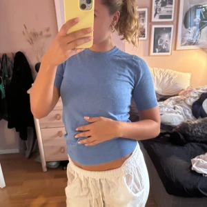 Blå kortärmad topp från Zara - Säljer en ljusblå topp från Zara i storlek S. Den har korta ärmar, rund hals och tre snygga guldfärgade knappar bak i nacken. Materialet är mjukt och stretchigt, perfekt för en chill och stilren look. Passformen är normal och toppen är enkel att matcha med jeans eller kjol.