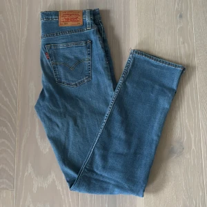 Levi's 501 blå jeans  - Klassiska Levi's 501 jeans i blå denim med rak passform och fem fickor. Snyggt läderpatch bak i midjan och ikonisk röd Levi's-tag på bakfickan. Perfekt för dig som gillar tidlös stil och vill ha ett par jeans som funkar till allt. Priset går att diskutera och vid frågor är det bara att höra av sig. Storleken är 14A. 