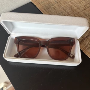 CHIMI 005 - Snygga solglasögon från Chimi i modellen COCO #005 med fyrkantig form och transparent brun båge. Glasen är tonade i brunt och bågarna är tillverkade i slitstark plast. Kommer med vit hårt fodral med text på insidan. Perfekt för dig som gillar stilrena accessoarer.