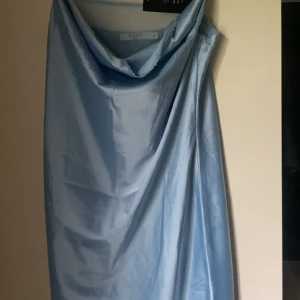 Ljusblå satin klänning med slits - Supersnygg ljusblå klänning från NA-KD i glansig satin och slits. Klänningen har justerbara axelband och glittrigt mesh tyg på insidan. Tycker att den är liten i storleken. Endast provad. Lappen sitter kvar. 