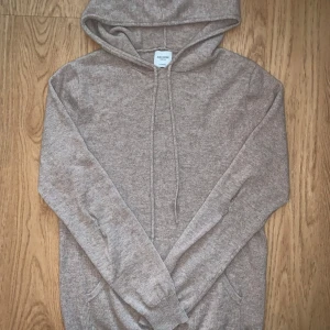 Beige cashmere hoodie från John Henric - Mjuk och lyxig beige hoodie i 100% cashmere från John Henric. Tröjan har huva med snörning, känguruficka och långa ärmar. Perfekt för dig som vill ha en stilren och bekväm look med exklusiv känsla. Lagad i armbågarna men inget som syns vid användning 