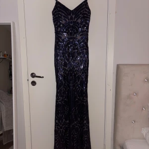 Mörkblå glittrig balklänning  - Säljer en superfin långklänning i mörkblått med glittriga paljetter och smala axelband. Klänningen har ett unikt mönster och en snygg v-ringning. Perfekt för dig som vill sticka ut på bal eller fest! Materialet känns lyxigt och skimrar snyggt i ljuset. Använd en gång, köptes på Infiny paris i Kista Gallerian. Köptes för ungefär 700-800kr