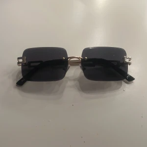 Svarta rektangulära solglasögon - Snygga solglasögon med rektangulära svarta glas och guldfärgade metallbågar. Med guldiga sidor. Pefrekt till dig som vill ha en cool look!