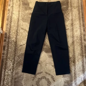 Mörkblå kostymbyxor från LCW Vision - Stilrena svarta kostymbyxor från LCW Vision i storlek 36. Byxorna har hög midja, raka ben och stängs med knapp och dragkedja. Perfekta för en clean och klassisk look. Materialet känns mjukt och följsamt, och de har diskreta fickor framtill.