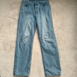 Levi's 501 90’s ljusblå jeans straight fit - Klassiska Levi's 501 jeans i ljusblå denim i lightweight, med rak passform och femficksdesign. Byxorna har knappgylf, ikonisk röd Levi's-tagg på bakfickan och läderpatch bak i midjan. Perfekta för en avslappnad och tidlös stil. Köpta i Maj och endast tvättade.