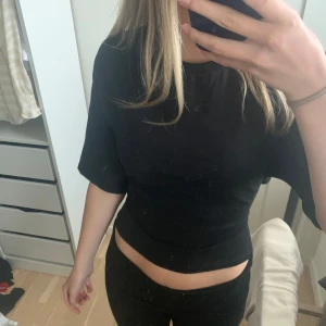 Svart topp med öppen rygg - Säljer en svart omlottopp med korta ärmar och snygg öppen rygg som knyts baktill. Toppen är knappt använd och är från nelly, storlek s!💞