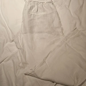 Vita linnebyxor från Zara med snörning - Snygga vita linnebyxor från Zara i storlek L. Byxorna har elastisk midja med snörning, bälteshällor och fickor fram och bak. Perfekta för en chill och luftig stil under varma dagar. Observera hål vid bakfickor. 