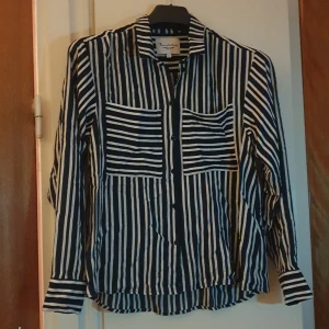 Randig skjorta från Bondelid, stl S - Snygg skjorta från Bondelid i svart och vitt med vertikala och horisontella ränder. Klassisk krage, långa ärmar och knäppning framtill. Skjortan har två bröstfickor och är tillverkad i ett mjukt bomullstyg. Perfekt för en stilren look.