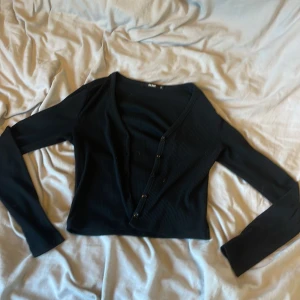Svart ribbad topp från Bik Bok - Svart långärmad topp från Bik Bok i ribbad bomullsmix. Djup v-ringning med knappar framtill ger en snygg och enkel look. Perfekt croppad längd som passar till både jeans och kjol. Enkel att styla och superbekväm.