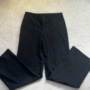 Svarta kostymbyxor med raka ben - Snygga svarta kostymbyxor med hög midja och raka, vida ben. Klassisk design med knapp och dold dragkedja framtill. Perfekta för en clean och stilren look. Materialet känns slätt och mjukt.