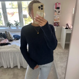 Mörkblå stickad tröja - Mysig mörkblå stickad tröja med rund halsringning och lång ärm. Tröjan har en enkel och klassisk design, perfekt för lager-på-lager och chill dagar. Den är fluffig och mjuk, vilket gör den extra skön att bära under kyliga månader.