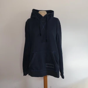 Mörkblå hoodie från Adidas med huva - Mysig mörkblå hoodie från Adidas med klassisk känguruficka och dragsko i huvan. Tröjan har Adidas-logga framtill.