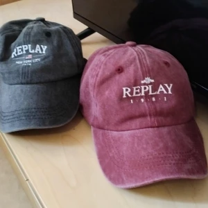 Replay kepsar i svart och vinrött - Två snygga kepsar från Replay, en i mörkgrå och en i vinröd ton. Båda har klassisk böjd skärm och vit broderad logga framtill. Tillverkade i mjuk bomull med justerbar rem bak för perfekt passform. Perfekt för dig som gillar streetstyle och vill ha en cool accessoar.