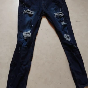 Mörkblå ripped skinny jeans - Säljer ett par mörkblå skinny jeans med rejält slitna och trasiga detaljer på båda benen. Jeansen har klassisk femficksdesign och är tillverkade i stretchigt denimtyg för en tight passform. Perfekta för dig som gillar en edgy och trendig look.