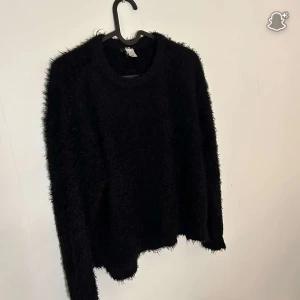 Svart fluffig stickad tröja H&M Divided - Mysig svart stickad tröja från H&M Divided i storlek M. Tröjan har en fluffig och lite lurvig yta som ger en cool och trendig look. Rund halsringning och långa ärmar, perfekt för lager-på-lager under kyliga dagar.