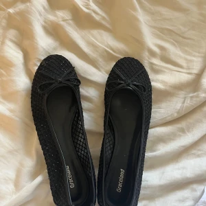 Svarta ballerinaskor från Graceland - Snygga svarta ballerinaskor från Graceland med diskret glittrig yta och rutmönster. Skorna har rund tå, liten rosett framtill och platt sula. Perfekta för dig som vill ha en stilren men ändå lite extra detalj på fötterna.