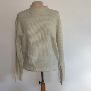 Beige stickad tröja från Uniqlo - Säljer en beige stickad tröja från Uniqlo i storlek M. Tröjan har en rak passform, ribbad struktur och högre rund halsringning. Tyvärr är halsen något uttöjd