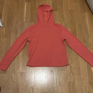 Korallfärgad hoodie med huva - Enkel och snygg korallfärgad hoodie från C i storlek 158/164. Tröjan har lång ärm och en klassisk huva, perfekt för chill dagar. Mjuk och skön, passar dig som gillar en basic stil utan massa detaljer.