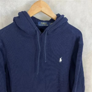 Mörkblå hoodie från Polo Ralph Lauren - Mörkblå hoodie från Polo Ralph Lauren med klassisk broderad logga på bröstet. Tröjan är stickad i bomull alltså en supersnygg och superbrkväm tröja, den har huva med snörning och en stor magficka. Perfekt för dig som gillar en chill och stilren look. Ordinarie pris 2700 mitt pris 700