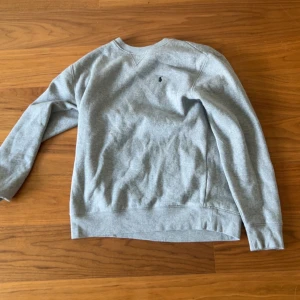Grå sweatshirt från Polo Ralph Lauren - Klassisk grå sweatshirt från Polo Ralph Lauren i storlek XL. Passar S i herr. Tröjan har rund halsringning, lång ärm och en liten broderad logga på bröstet. Tillverkad i mjuk bomullsblandning som är perfekt för kyligare dagar.