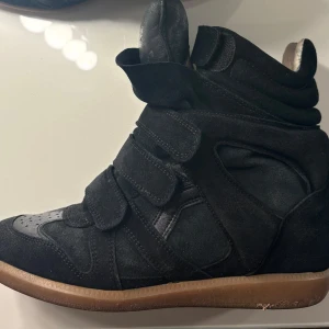 Isabel Marant Bekett sneakers – Svarta - Säljer mina klassiska Isabel Marant Bekett wedge sneakers i svart mocka och skinn. Storlek: 40 (normala i storlek) Färg: Svart med gummisula Detaljer: Dold kilklack, kardborreband, rund tå, mjukt innerfoder i skinn. Kommer med original dustbags.  Skorna är i fint använt skick – sulan visar viss användning och det finns lite tecken på användning i skorna (se bilder). Ovandelen är dock välbevarad.  Nypris ca 6 000 kr.  💌 Skicka gärna ett meddelande vid frågor eller om du vill ha fler bilder! 