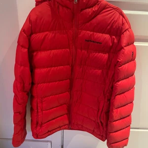 Röd Peak Performance dunjacka L - Riktigt snygg röd dunjacka från Peak Performance i storlek L. Jackan har huva, dragkedja framtill och klassisk pufferstil. Perfekt för kalla dagar och ger en cool look med sin starka färg och quiltade design.