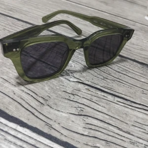 Gröna solglasögon Kiwi - Snygga solglasögon från Kiwi med transparent grön båge och mörka fyrkantiga linser. Ramen är i plast och har en cool, modern vibe som sticker ut. Perfekta för dig som vill ha en unik accessoar till sommaren.